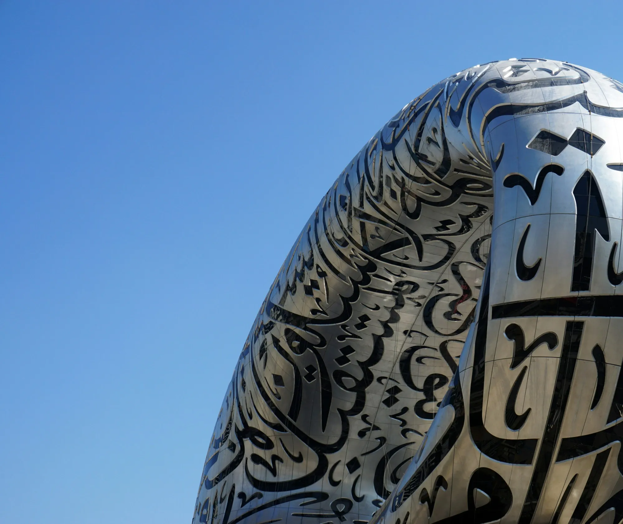 Stainless-steel facade of the Museum of the Future in Dubai, carved with Arabic calligraphy against a clear blue sky